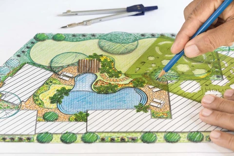 Main d'architecte paysagiste dessinant un plan d'aménagement extérieur coloré avec crayon bleu