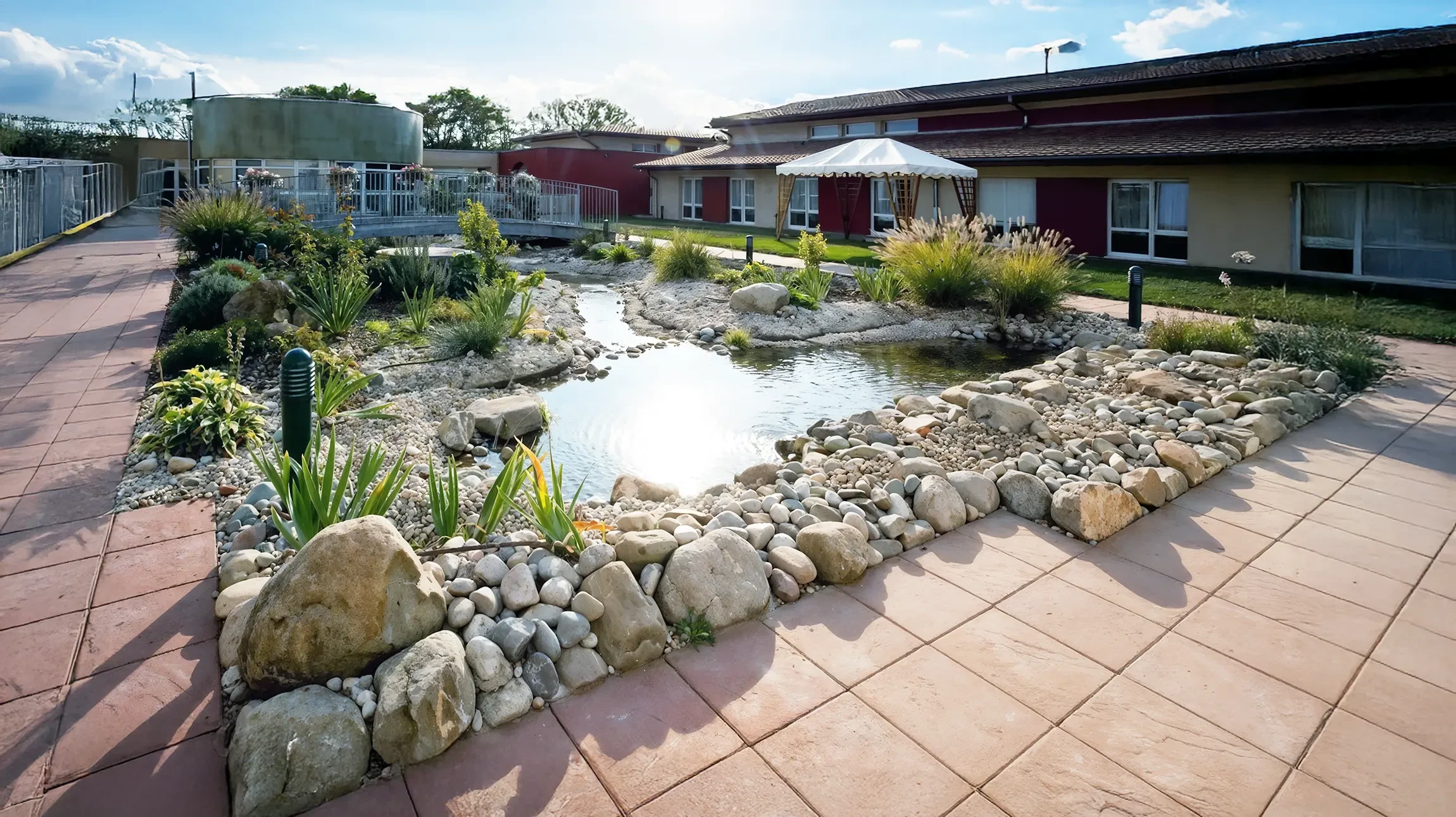Jardin paysager avec pelouse impeccable, massifs de vivaces et arbustes ornementaux, allée en pavés courbes, escalier en pierre naturelle et murs de soutènement en brique et pierre